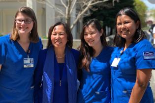 Nursing students in blue scrubs with President Judy K. Sakaki