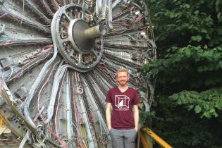 Physics student stands in front of large piece of particle physics hardware at CERN
