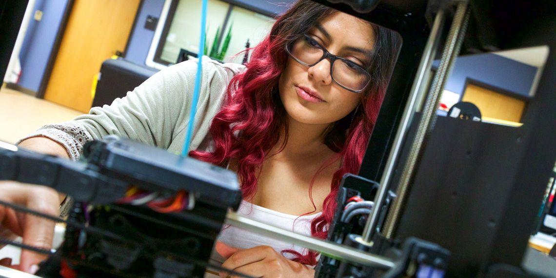 A student, in the background, uses a 3D printer, in the foreground