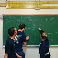 Three math students write with chalk on a chalkboard