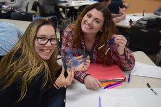 One student holds up a protractor while another student holds a compass
